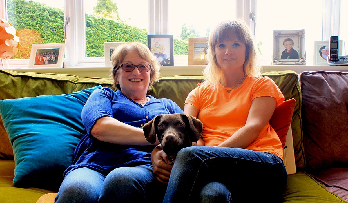 Two women are sitting on a sofa - with a brown dog